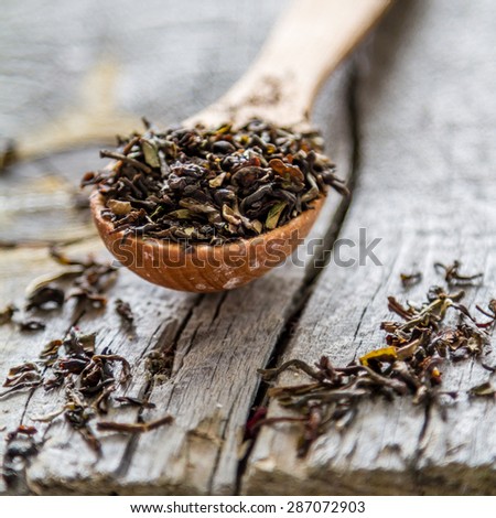 Black dry tea, wood spoon, rustic wood background, closeup
