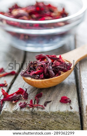 Dry hibiscus tea in glass bowl and wood spoon, rustic wood background
