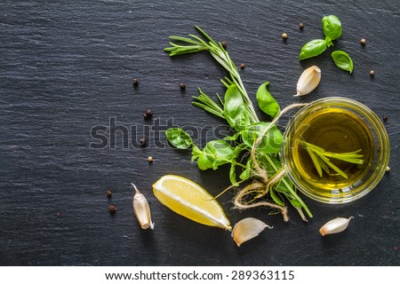 Herbs background - rosemary, basil, mint, lemon, olive oil, garlic, pepper, dark stone background, top view