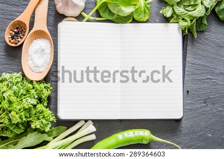 Cooking book - mint, parsley, arugula, spinach, onion, chili, garlic, dark stone background, top view