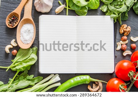 Cooking book - mint, parsley, arugula, spinach, onion, chili, garlic, tomatoes, nuts, dark stone background, top view