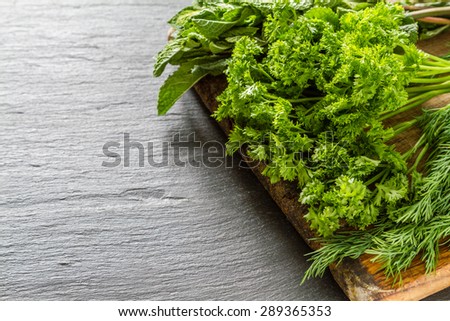Herbs background - parsley, mint, dill, onion, wood board, dark stone background, closeup