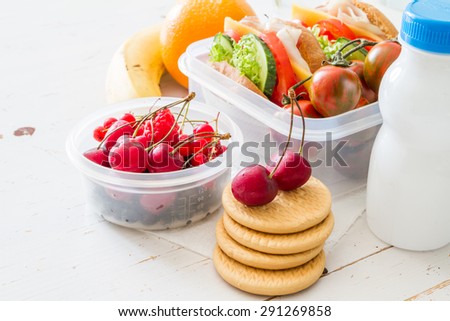 Lunch box - sandwiches, tomatoes, berries, cookies, milk, fruits, white wood background