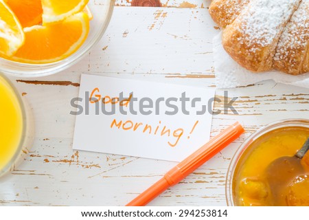Good morning note, breakfast - croissant, juice, oranges, white wood background, top view