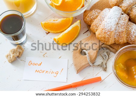 Good morning note, breakfast - croissant, coffee, jam, juice, oranges, white wood background, top view