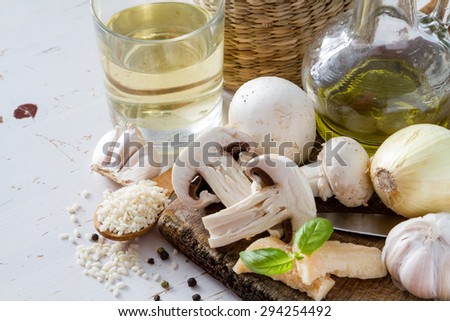 Risotto ingredients - rice, mushrooms, oil, wine, cheese, garlic, onion, white wood background