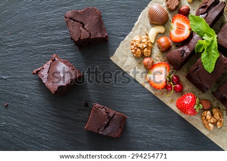 Brownie, nuts, strawberry, mint, candy, baking paper, dark stone background, top view