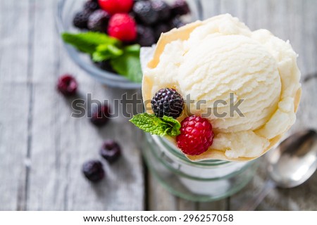 Vanilla ice cream in waffle cone with raspberry and blackberry, mint, rustic wood background