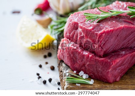 Raw meat, rosemary, salt, pepper, garlic, lemon, wood background