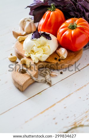 Caprese salad ingredients - tomato, mozzarella, basil, nuts, oil, white wood background