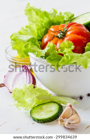 Salad ingredients - lettuce, tomato, cucumber, onion, garlic, oil, white wood background