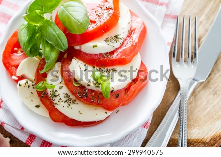 Insalata caprese - tomato, mozzarella, basil, olive oil, white plate, rustic wood background