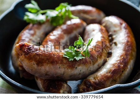 Grilled sausages on pan with herbs and spices, wood background, closeup