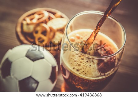 Pouring beer into glass with snacks and football