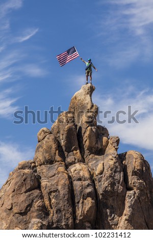 Male climber waves an American flag on the summit of a mountain.