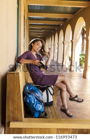 Young woman sitting on a bench with her bags waiting for a ride at a depot.