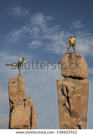 Team of male climbers conquer the summit of a challenging rock spire.