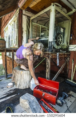 Attractive woman fixing a swamp cooler in a rustic cabin.