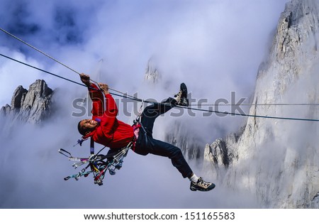Male, ethnic rock climber pulls himself across a tyrollean traverse.