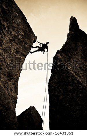 A rock climber is silhouetted against the evening sky as he rappels past an overhang in Joshua Tree National Park.