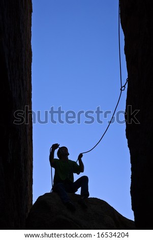 Rock climber silhouetted as he belays his partner up a chimney in Joshua Tree National Park.