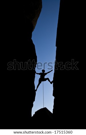 Rock climber silhouetted as he climbs up a chimney in Joshua Tree National Park, California, on a summer day.