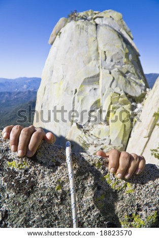 Rock climbers hands gripping the edge of a cliff in the Sierra Nevada Mountains, California, on a sunny day.