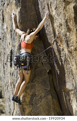 Female climber ascending a steep rock face in Joshua Tree National Park on a sunny day.