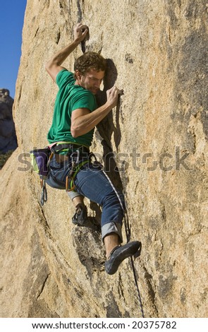 Climber ascending a steep rock face in Joshua Tree National Park on a sunny day.