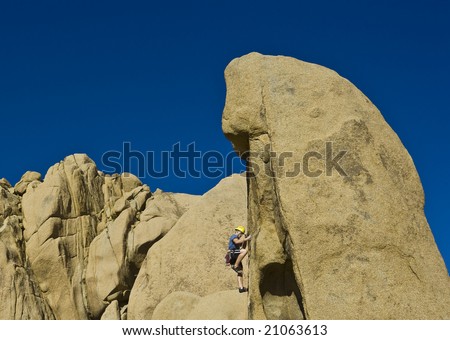 A rock climber ascends a steep rock face in Joshua Tree National Park, California, on a sunny day.