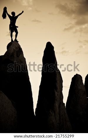 Rock climber silhouetted on the summit of a rock spire in Joshua Tree National Park, California, on a summer day.
