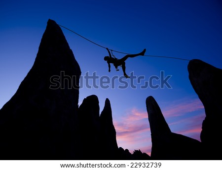 A climber is silhouetted as she pulls herself across a gap between two pinnacles, in the Sierra Nevada  Mountains, California.