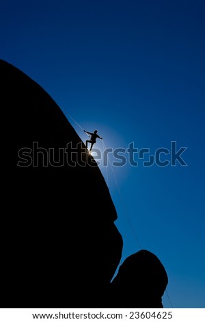 A climber is silhouetted as rappels down a steep rock face in the Sierra Nevada Mountains, California.
