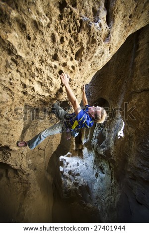 Climber grips the rock and clings to an overhanging cliff as he prepares for his next move on Sandia Rock, California.