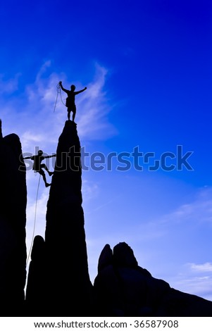 A team of climber is silhouetted against the evening sky as they ascend a steep rock face in Joshua Tree National Park, California.