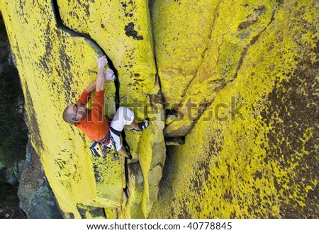A male climber is determined to ascend a difficult hand and fist crack on a sheer rock face.