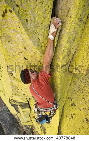 A male climber is determined to ascend a difficult hand and fist crack on a sheer rock face.