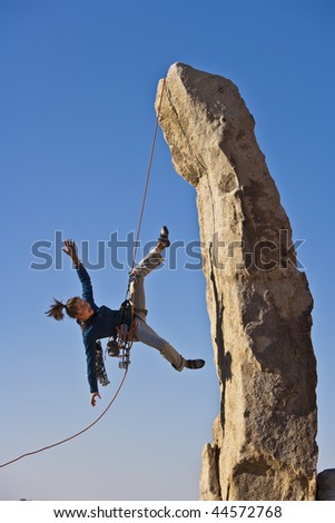 Climber in trouble dangling from her rope as she scales a rock pinnicle in the remote Mojave Desert of California.