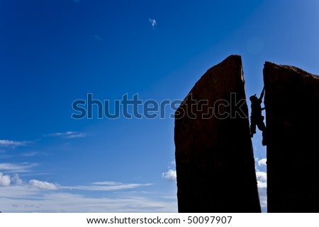 Rock climber squeezes his body between a gap in the summit of a split spire.