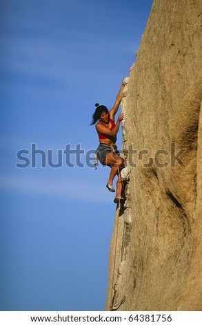 Female rock climber struggles for her next grip on the edge of a steep cliff.