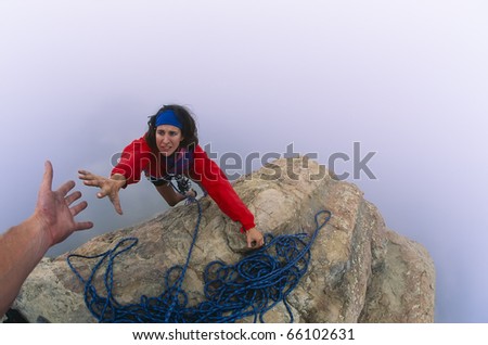 Rock climber on the summit reaching for a helping-hand from her partner.