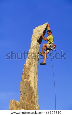 Rock climber struggles for his next grip on a overhanging pinnacle.
