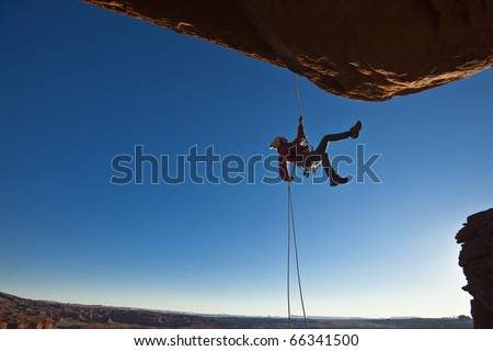 Rock climber dangles in midair as she  rappells past an overhang.