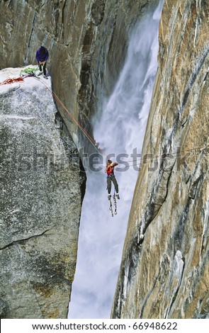Team of climbers reaching the summit of The Lost Arrow Spire, in Yosemite National Park, by tyrolean traverse as Yosemite Falls roars behind them.