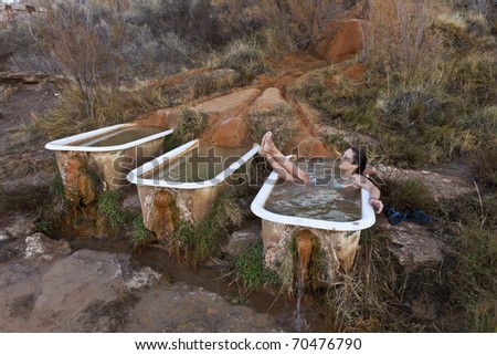 Young woman soaking in the rustic and funky Mystic Hot Springs,  the calcium rich water deposits create the organic textures flowing over the ground and into a recycled claw foot bathtub.