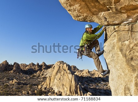 Male rock climber struggles for his next grip as he clings to a sheer cliff.