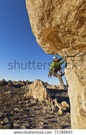 Male rock climber struggles for his next grip as he clings to a sheer cliff.