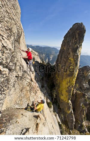 Team of climbers struggle for their next grip on a steep rock wall.