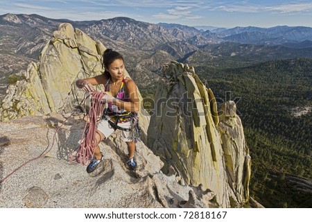 Female climber coiling ropes on the summit of a steep rock spire.