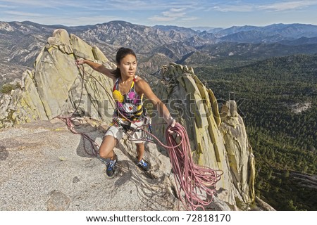 Female climber coiling ropes on the summit of a steep rock spire.